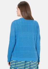 Blauer gestrickter Pullover mit geometrischen Mustern, strukturierten Abschnitten und festen Rippenbündchen. Die Rückansicht zeigt die Design- und Farbdetails.