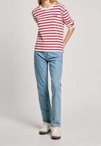 Cotton T-shirt with red and white horizontal stripes, featuring a small logo. Paired with light blue straight-leg jeans and white sneakers.