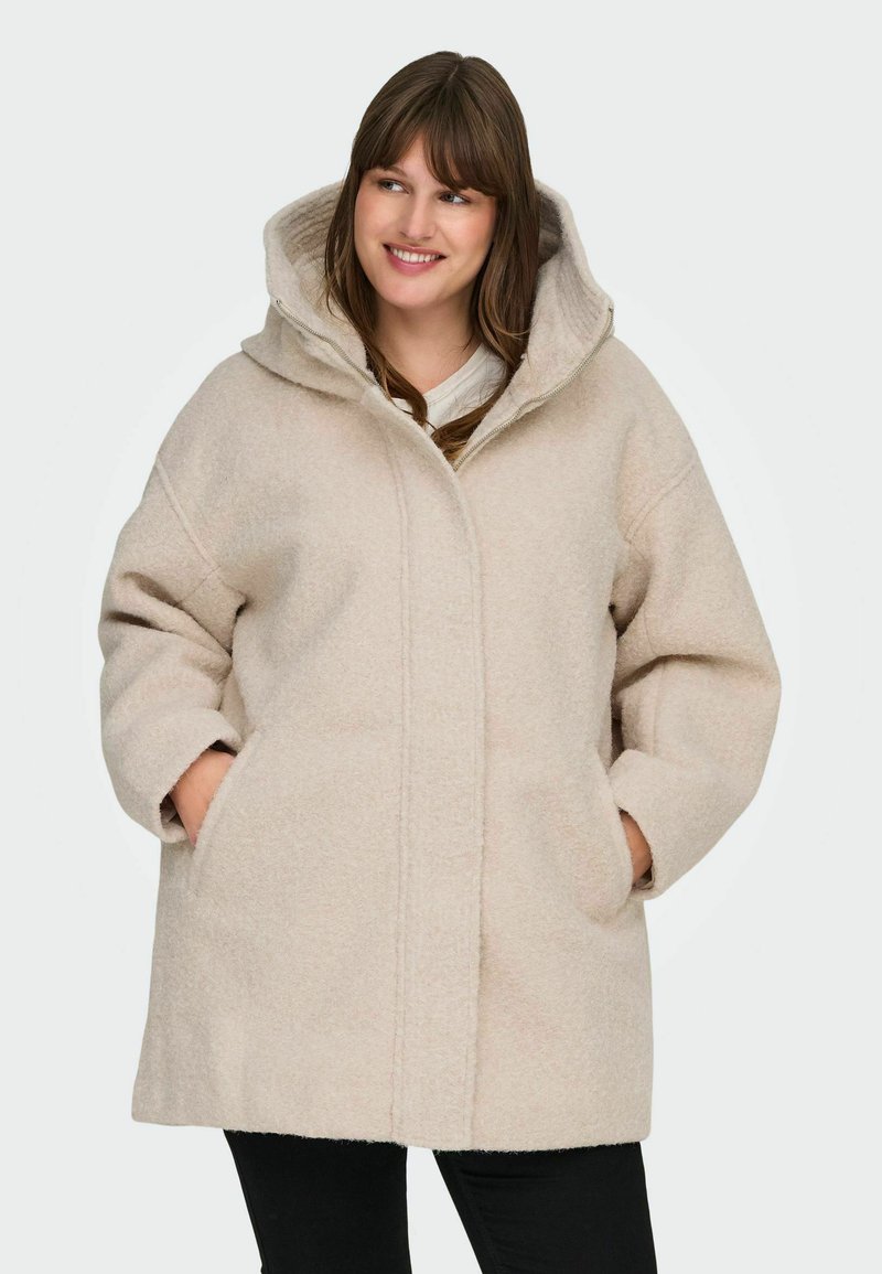 Bež villasegu mantel suure kapuutsiga, üleliia suuruse, küljetaskute ja pehme tekstuuriga, esiseemiga ja minimalistikus disainis.