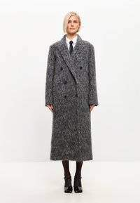 Abrigo de lana gris de mezcla, de doble botonadura, con un acabado texturizado, gran cuello de solapa y botones negros, que llega hasta media pantorrilla.