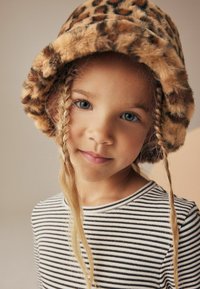 Leopardprint bucket hat med en blød, furry tekstur, parret med en langærmet skjorte med sort-hvide striber. Barn med fletninger.
