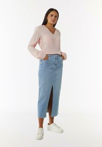 Lichtroze V-hals blouse met gathered mouwen, gecombineerd met een lichtblauwe denimrok met hoge taille en een split aan de voorkant, gedragen met witte sneakers.