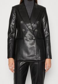 Blazer en cuir noir croisé avec de gros boutons, revers entaillés et deux poches latérales. Texture lisse avec des surpiqûres blanches contrastantes.