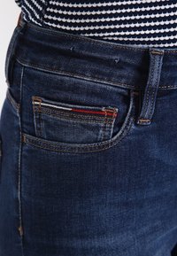 Mörkblå denimjeans med en figurnära design, som har en liten ficka och kontrasterande sömmar. Slät textur och hållbart material.