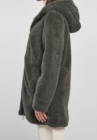 Šedá flísová mikina s kapsou, která má měkký, strukturovaný povrch, přední zip, boční kapsy a nastavitelný spodní okraj.