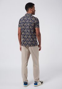 Camicia a maniche corte con base blu navy, caratterizzata da una stampa floreale gialla e crema. Abbinata a pantaloni beige e sneaker bianche.