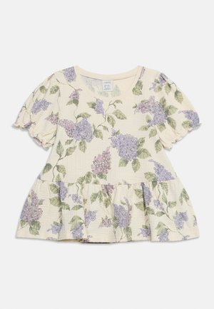 Blouse crème à manches courtes avec manches bouffantes et ourlet peplum, décorée de feuilles vertes et d'un imprimé floral lilas violet.