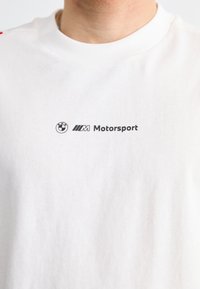Balta medvilnė marškinėliai su juodu BMW logotipo ir „M Motorsport“ tekstu spausdintu ant krūtinės. Klasikinio apvalaus kaklo dizainas.