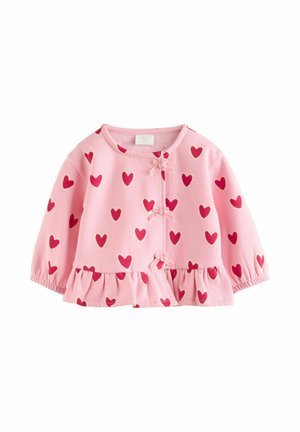 Bladoróżowy kardigan z falbaną u dołu, wzorem czerwonych serc, długimi rękawami oraz małymi dekoracyjnymi kokardkami przy zapięciach z przodu.