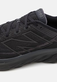 Schwarzer Laufschuh mit einem strukturierten Obermaterial aus Stoff, Gummisohle und einem auffälligen "N"-Logo. Schnürsenkel und verstärkte Ösen sind enthalten.