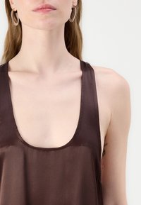 Brun sateng tanktopp med dyp utringning og tynne stropper. Har en jevn tekstur og minimalistisk design som fremhever enkelhet.