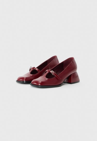 Chaussures en cuir bourgogne avec un bout arrondi, design à bride T et un distinctif talon bloc sculpté. Texture lisse et accents matériels minimaux.