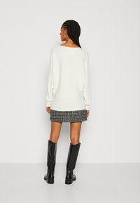 Pull en tricot blanc avec des manches larges, associé à une jupe noire et blanche à motif et des bottes en cuir noir jusqu'aux genoux.