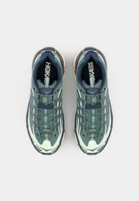 Zielono-kremowe buty sportowe z teksturowaną cholewką, panelami z siateczki oraz systemem sznurowania; wyposażone w wielokolorową gumową podeszwę.