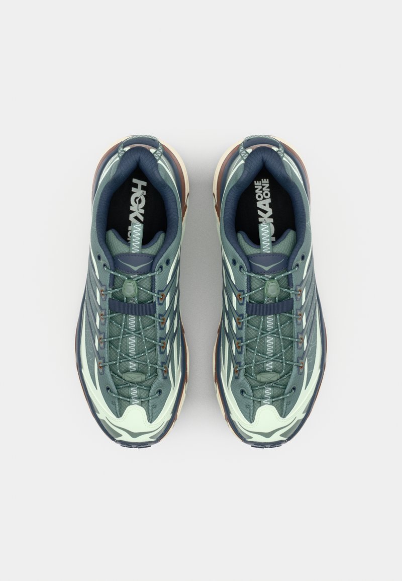 Gröna och krämfärgade träningsskor med en texturerad ovandel, nätpaneler och snörsystem; har en mångfärgad gummisula.