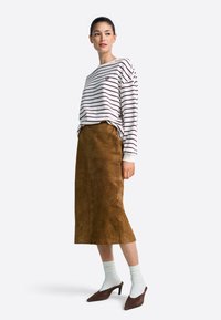 Maglietta a maniche lunghe a righe bianche e bordeaux, abbinata a una gonna midi in suede marrone, calzini bianchi a coste e scarpe con tacco marroni.