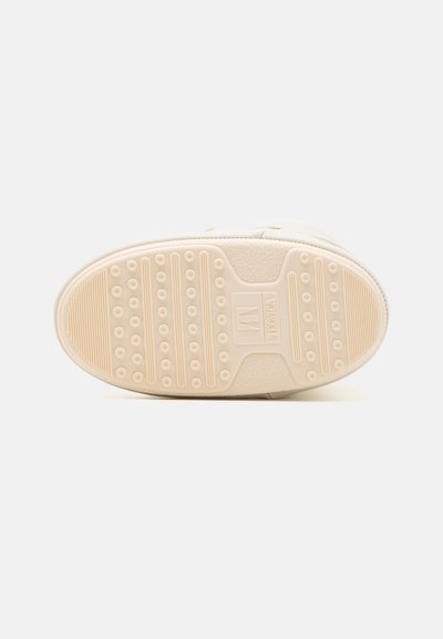 Beige sneakersula med texturerad gummi, med cirkulära greppmönster, en logotyp och horisontella linjer för grepp.