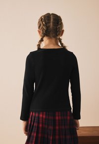 Haut noir à manches longues avec un col rond, associé à une jupe à carreaux rouges. Le haut est en tissu texturé et présente une silhouette ajustée.