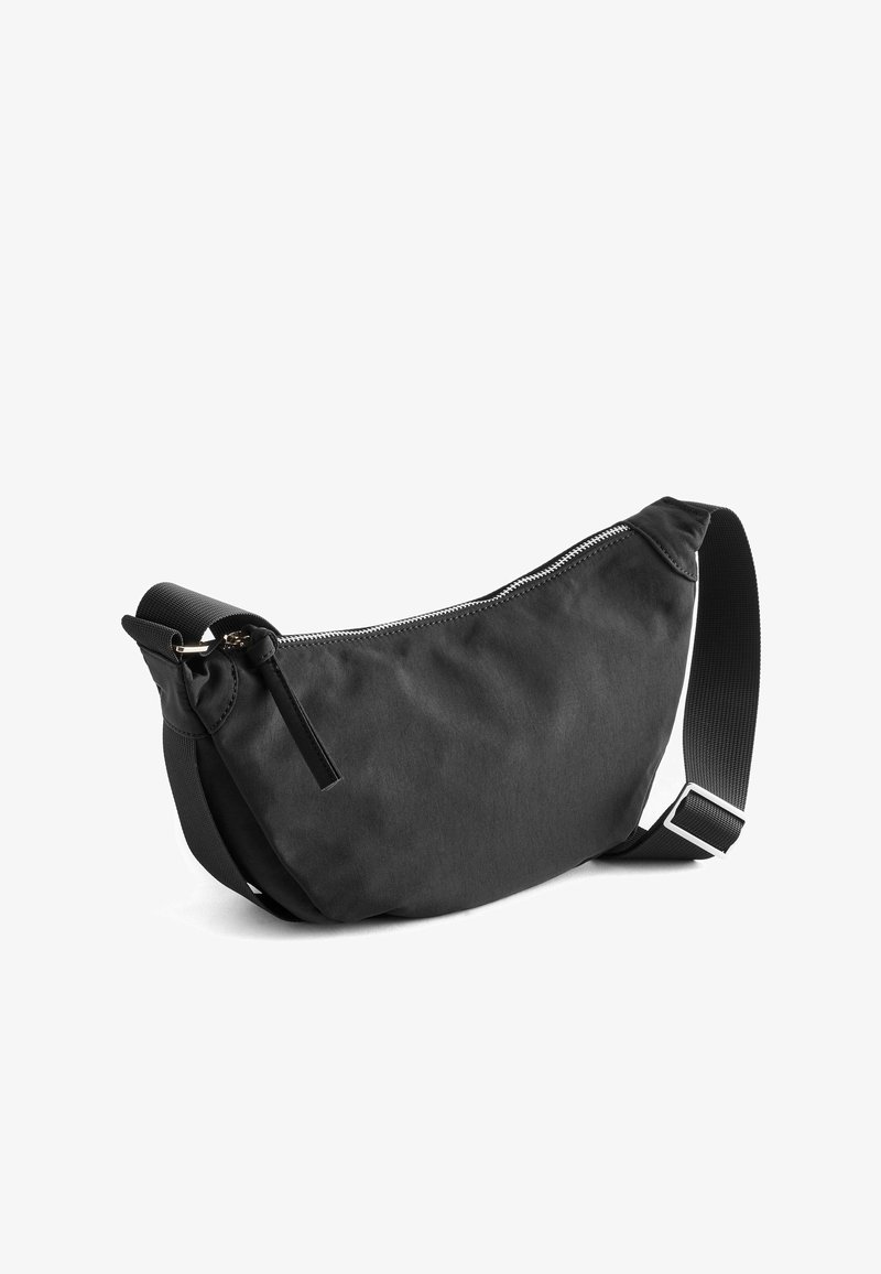 Schwarze Stoff-Schultertasche mit geschwungenem Schnitt, Reißverschluss und verstellbarem Trageriemen. Verfügt über eine glatte Textur und minimalistisches Design.