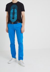 Czarny t-shirt z niebieskim wzorem graficznym, zestawiony z jasnoniebieskimi spodniami i białymi trampkami. Strój ma standardowy krój i gładkie tekstury.