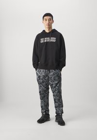 Black hooded sweatshirt with white text; paired with black and gray patterned pants featuring swirling designs; black athletic shoes.