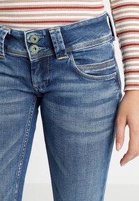 Modré džíny z denimu s vybledlým praním, s dvojitým zapínáním, pěti kapsami a viditelnými švy.