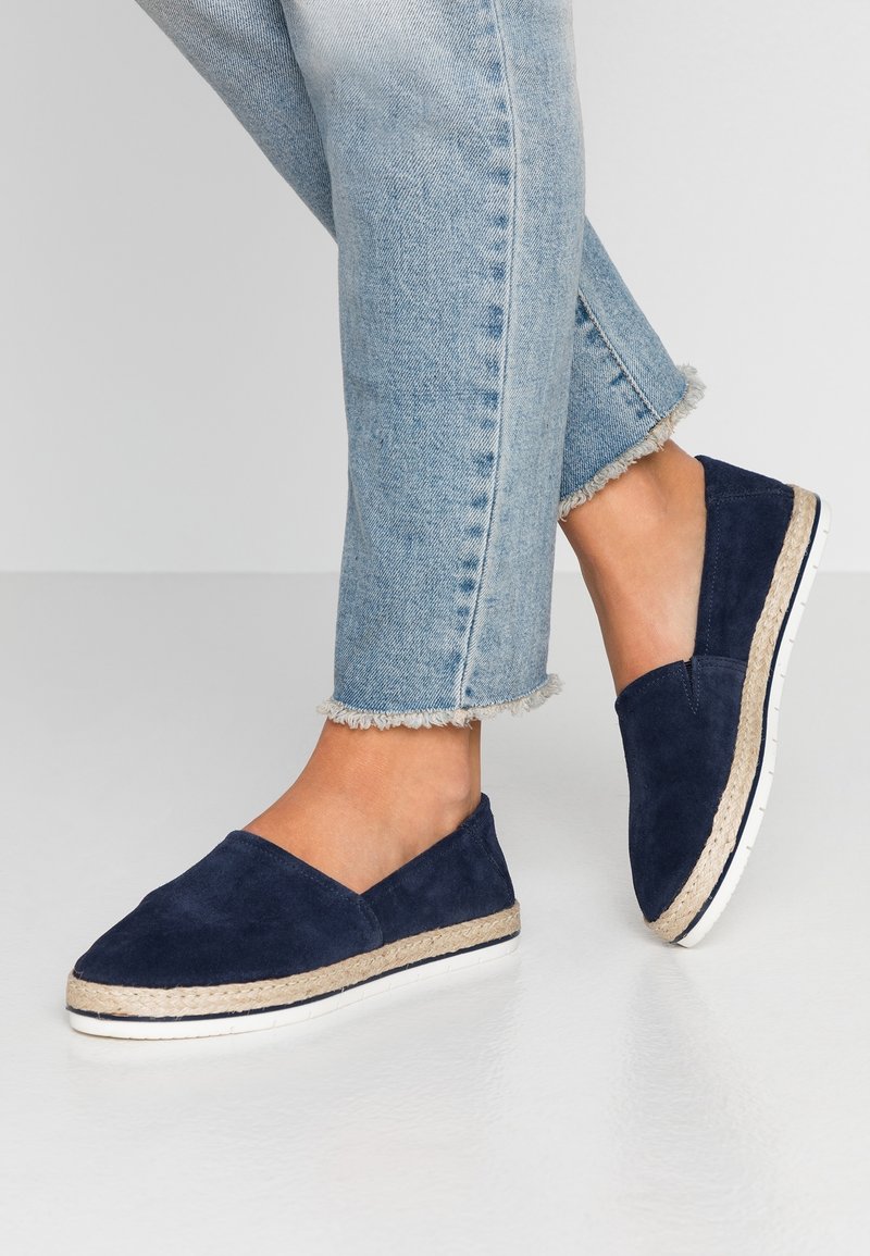 Marinblå mocka slip-on espadriller med en vävd jutesula och vit gummitrim, parat med avskurna jeans med fransar.