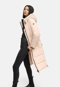 Long, puffy pink coat with a hood, featuring a front zipper and side pockets, paired with black skinny jeans and ankle boots. Smooth texture.