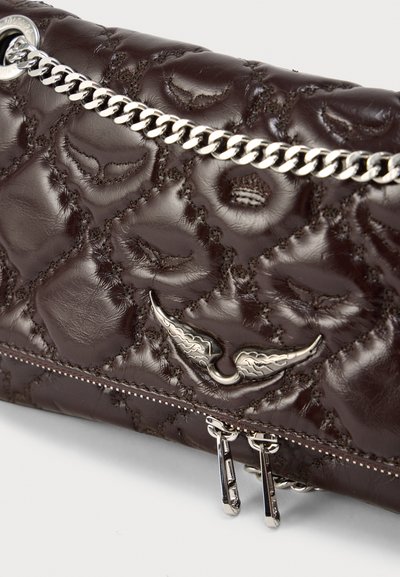 Ruda odinė delninė su siuvinėta tekstūra, sidabro spalvos grandinėlės dirželiu ir dekoratyviu metaliniu sparno formos akcentu. Turi dvigubą užtrauktuką.