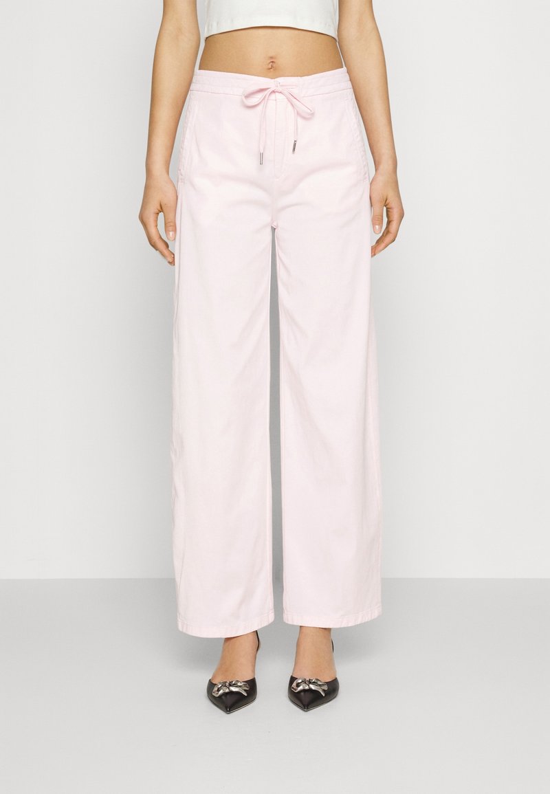 Lichtroze wijde broek met een drawstring tailleband, gemaakt van katoen. Heeft een soepele textuur en zijzakken. Gepaard met zwarte puntige schoenen.