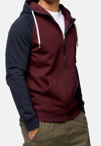 Ritssluiting hoodie met een kastanjebruine body en marineblauwe mouwen. Voorzien van een trekkoord capuchon, zijzakken en geribde manchetten, gemaakt van een zachte stof.