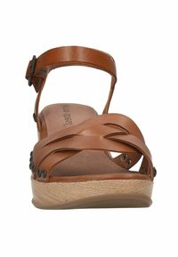 Brown leather sandal with crisscross straps and adjustable ankle strap. Features wooden platform sole and decorative metal studs on the sides.