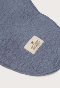 Modul vyrobený z modrého filcu s hladkým povrchom, zaobleným tvarom a prešitým okrajom. Obsahuje béžovú nálepku s nápisom "HUTTEGUT" a logom hviezdy.
