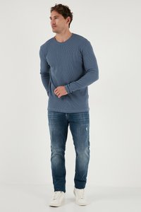 Modra rebrasta majica z dolgimi rokavi je kombinirana z raztrganimi kavbojkami in belimi športnimi copati. Majica ima okroglo ovratnico in prilega rokave.