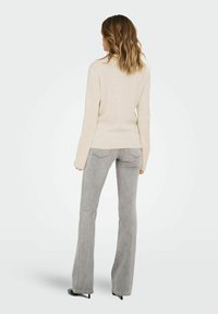 Beige geripptes Sweatshirt mit langen Ärmeln, kombiniert mit hellgrauen Schlagjeans. Das Outfit zeichnet sich durch eine figurbetonte Silhouette und subtile Steppdetails aus.