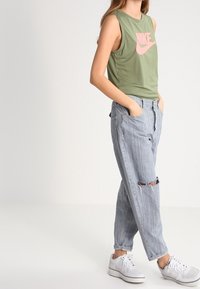 Grön ärmlös topp med rosa Nike-logga, ihopparad med ljusblå rivna jeans och vita sneakers. Avslappnad passform med synlig textur.