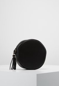 Černá kulatá taška z hladké umělé kůže s uzavíráním na zip a ozdobným střapcem. Jednoduchý, kompaktní design bez zdobení.