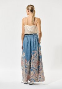 Blauwe maxi rok met bloemenprint, versierd met ingewikkelde beige en roze borduursels, uitgerust met een elastische tailleband en zijzakken, gecombineerd met een lichte tanktop.