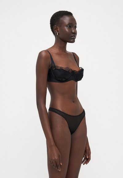 Soutien-gorge noir avec dentelle, en tissu lisse et bavettes réglables, associé à un string en maille transparente assorti, tous deux dotés de détails de couture délicats.