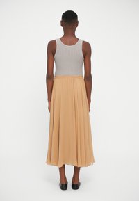 Beige pleated skirt with an elastic waistband, paired with a gray ribbed tank top. The fabric appears soft and lightweight. Black slip-on shoes.