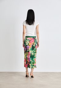 Sukně s květinovým potiskem a zeleným páskem, s multikolorovanými květinami v odstínech růžové, žluté a zelené; spárovaná s bílým vrchním dílem s žebrováním.