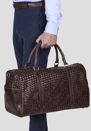 Brown woven leather duffel bag featuring double handles, silver hardware, and a side pocket, presented against a neutral background.
