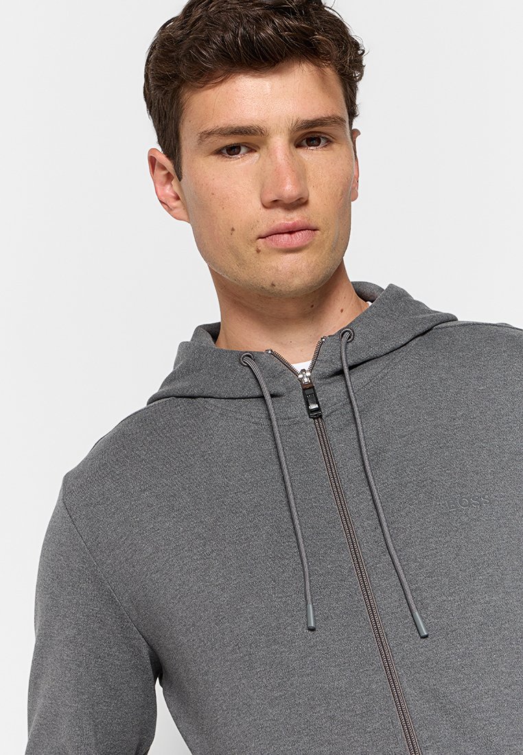 Grijze zip-up hoodie met een gestructureerde afwerking, capuchon met trekkoord en subtiele logo-details op de borst. Heeft een gestroomlijnd ontwerp en praktische ritsen.