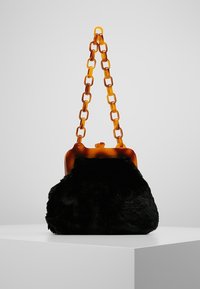 Černá plyšová kabelka s řetízkem a zavíráním z jantarového želvovinového vzoru. Měkká textura, zaoblený tvar a strukturální horní rám.