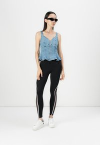 Denim peplum top with a front zipper and flared hem, paired with black leggings featuring white side stripes. Model wears white sneakers.