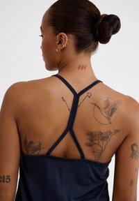 Marinblå atletisk linne med racerback-design, med texturerad tyg och flera tatueringar på ryggen, inklusive en trana och ett hjärta.