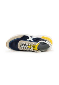 Navy and beige sneaker with white accents, featuring a textured upper, flat laces, yellow detail on the heel, and a gum rubber outsole.
