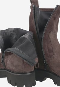 Bottines en suède marron avec une semelle en caoutchouc noir, présentant des fermetures éclair et un doublure en tissu texturé pour un enfilage facile.