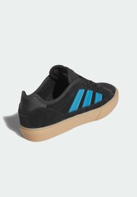 Čierna semišová teniska s modrými tromi pruhmi, podrážkou z gumovej gumy a polstrovaným golierom. Má šnurovací dizajn a textúrované látkové akcenty.