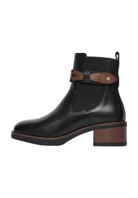 Bota negra de tobillo con tacón apilado marrón, paneles laterales elásticos y tira decorativa de cuero marrón con detalle de botón dorado.